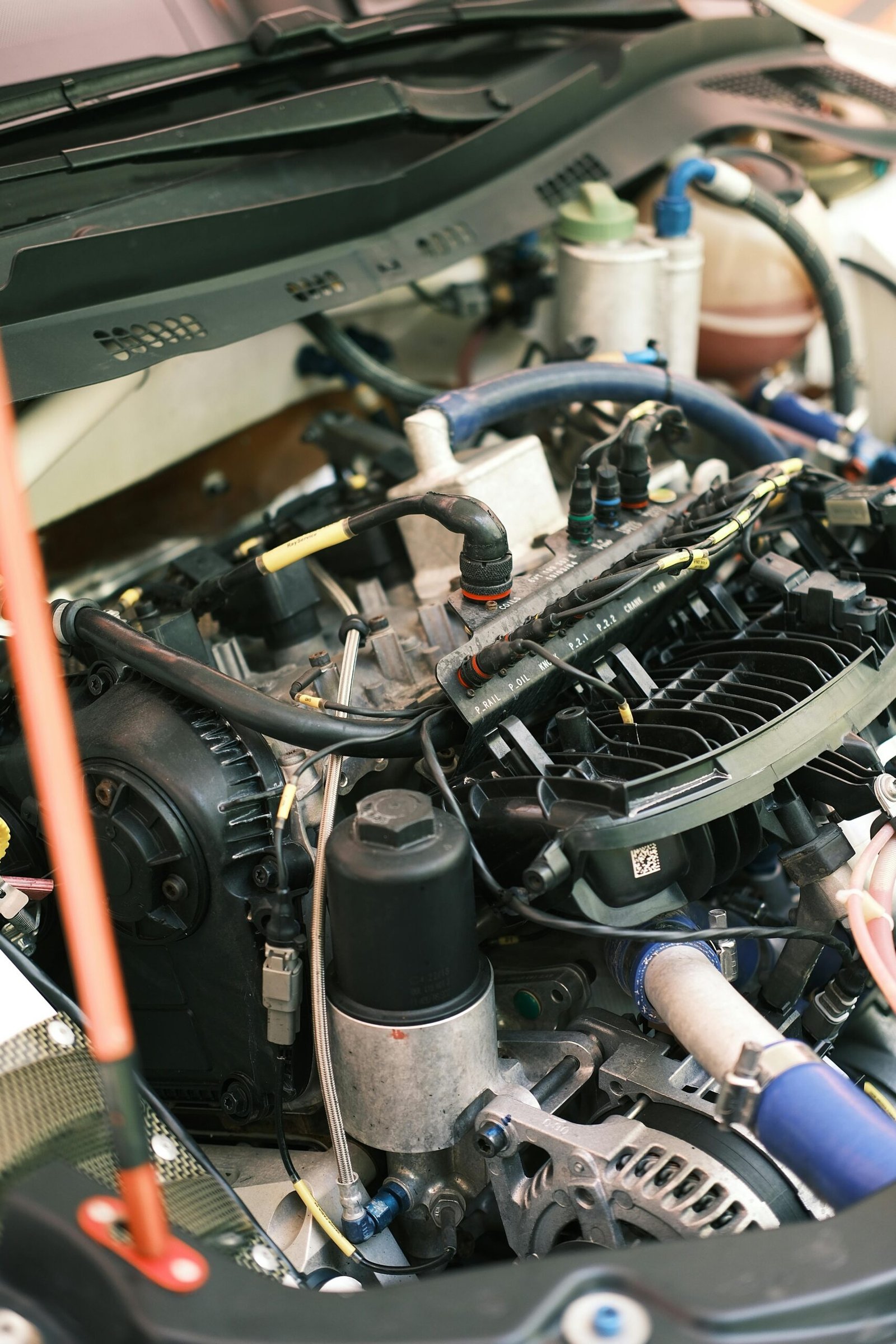 Open car hood showing a detailed view of a complex engine system with blue hoses, aluminum components, and electrical wiring.